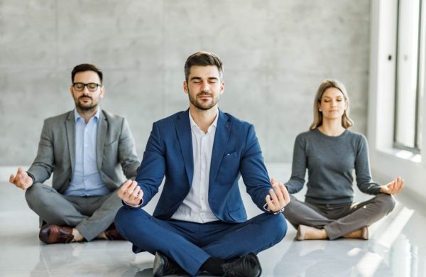 Group of business people meditating in Lotus position on the floor at casual office. Copy space.